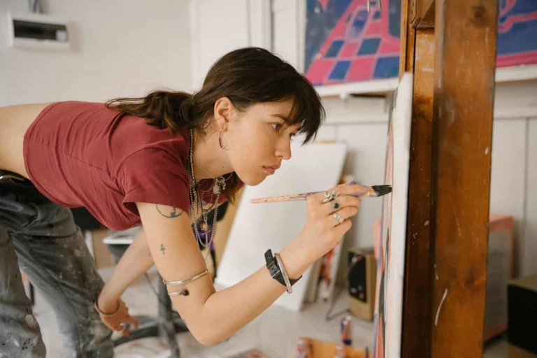 concentrated-young-woman-bending-over-and-drawing-on-canvas-3959079
