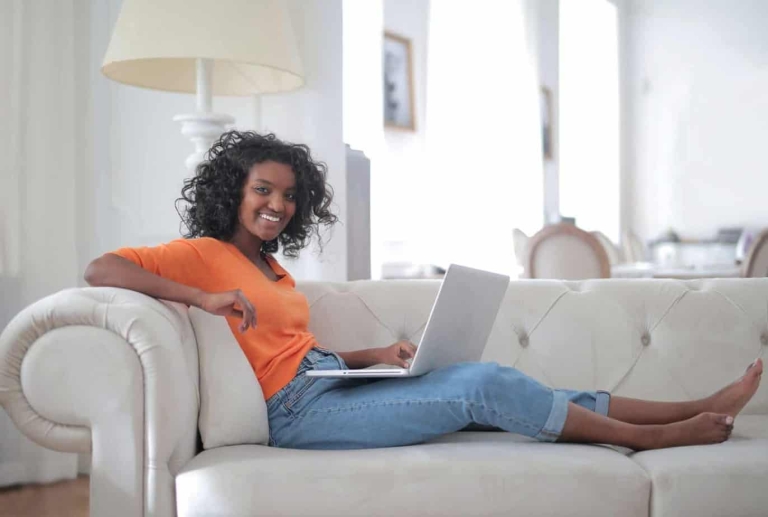 positive-young-ethnic-lady-sitting-on-sofa-with-laptop-and-3961198